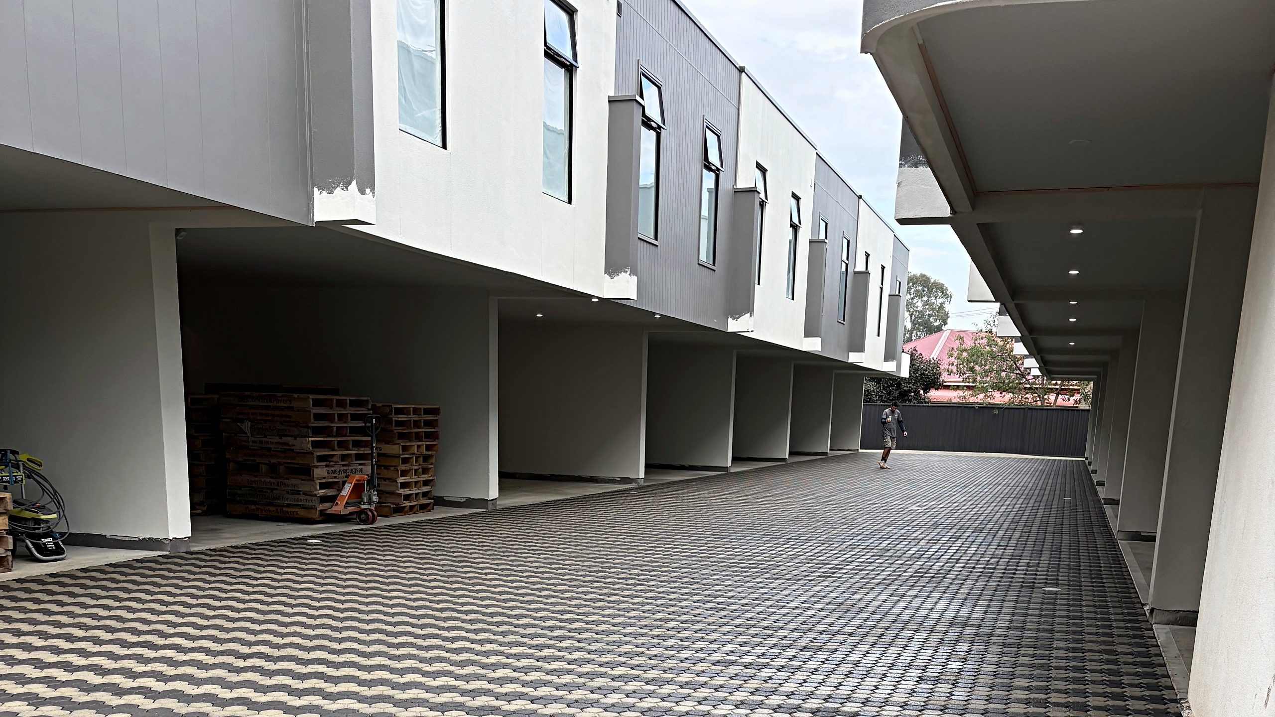 A shared driveway of charcoal and bone hexagonal pavers running the length of a row of townhouse carports.