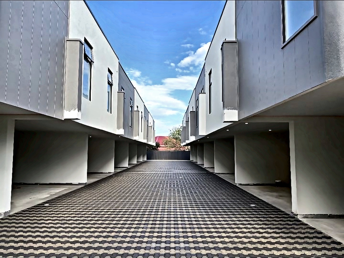 Shared driveway of charcoal and grey pavers running between two rows of townhouses.