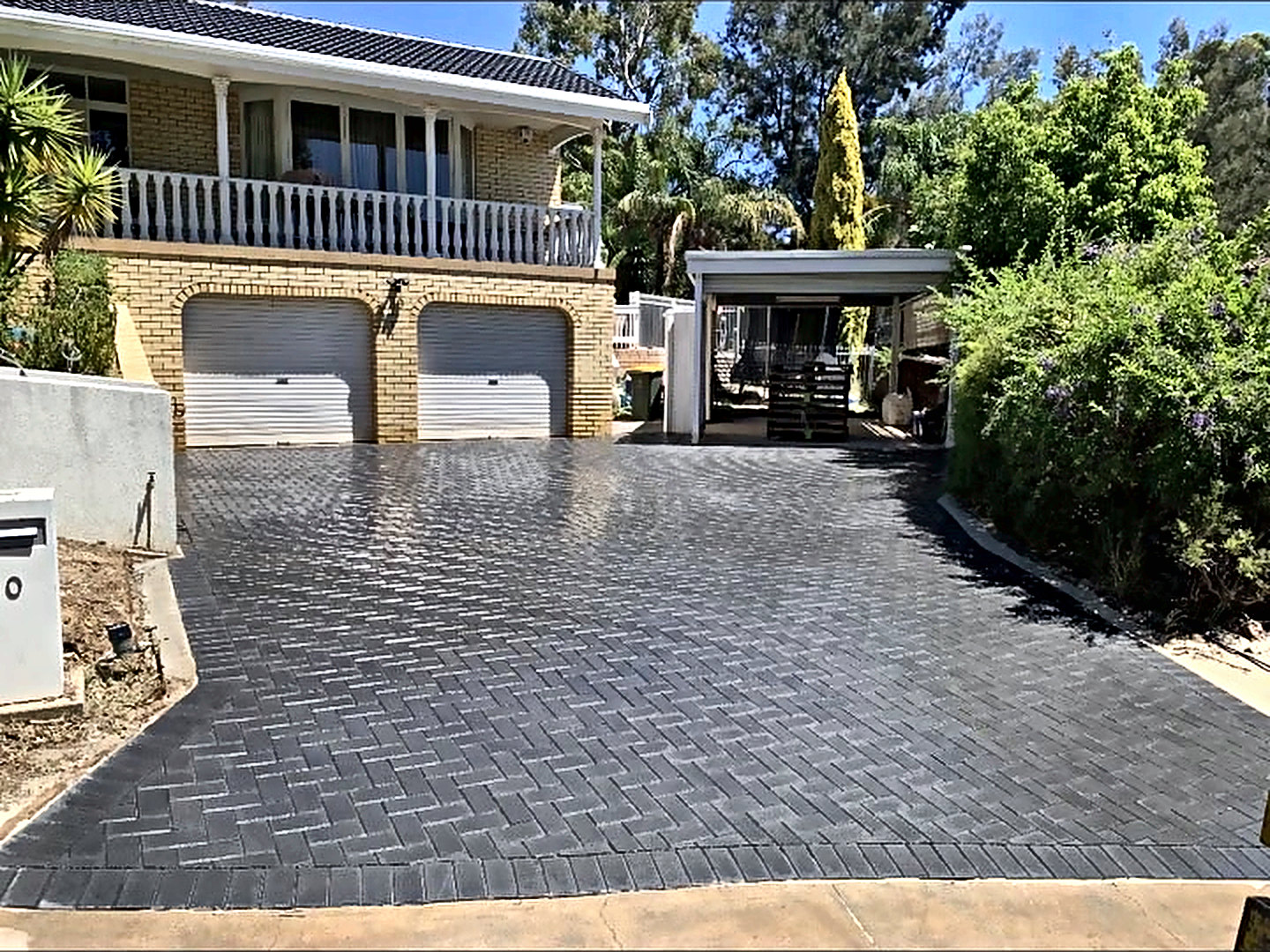 Wide charcoal herringbone paved driveway sweeping up to a double garage.