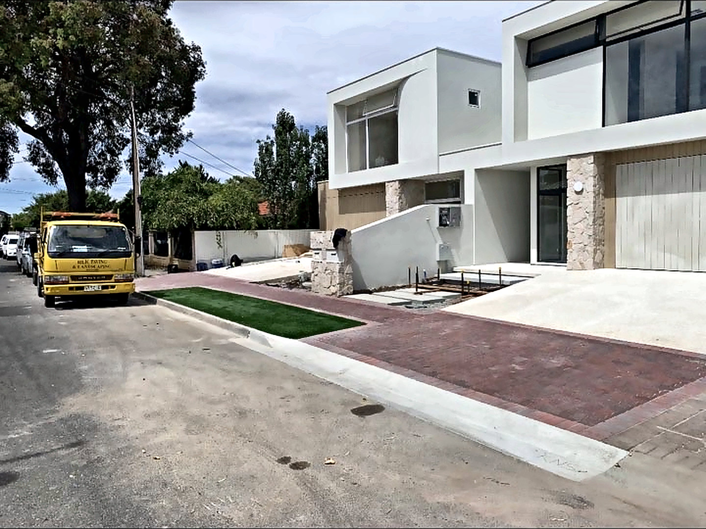 Red paved driveway and crossover finished in front of a white rendered two-storey home.