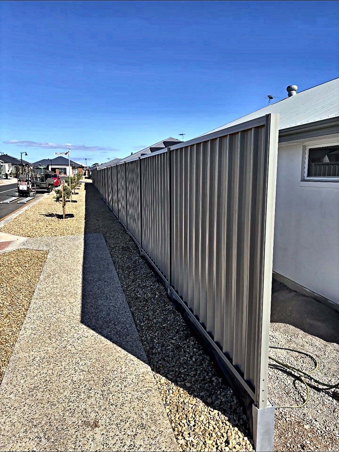 Long run of colorbond boundary fencing beside an exposed aggregate path and decorative stone.
