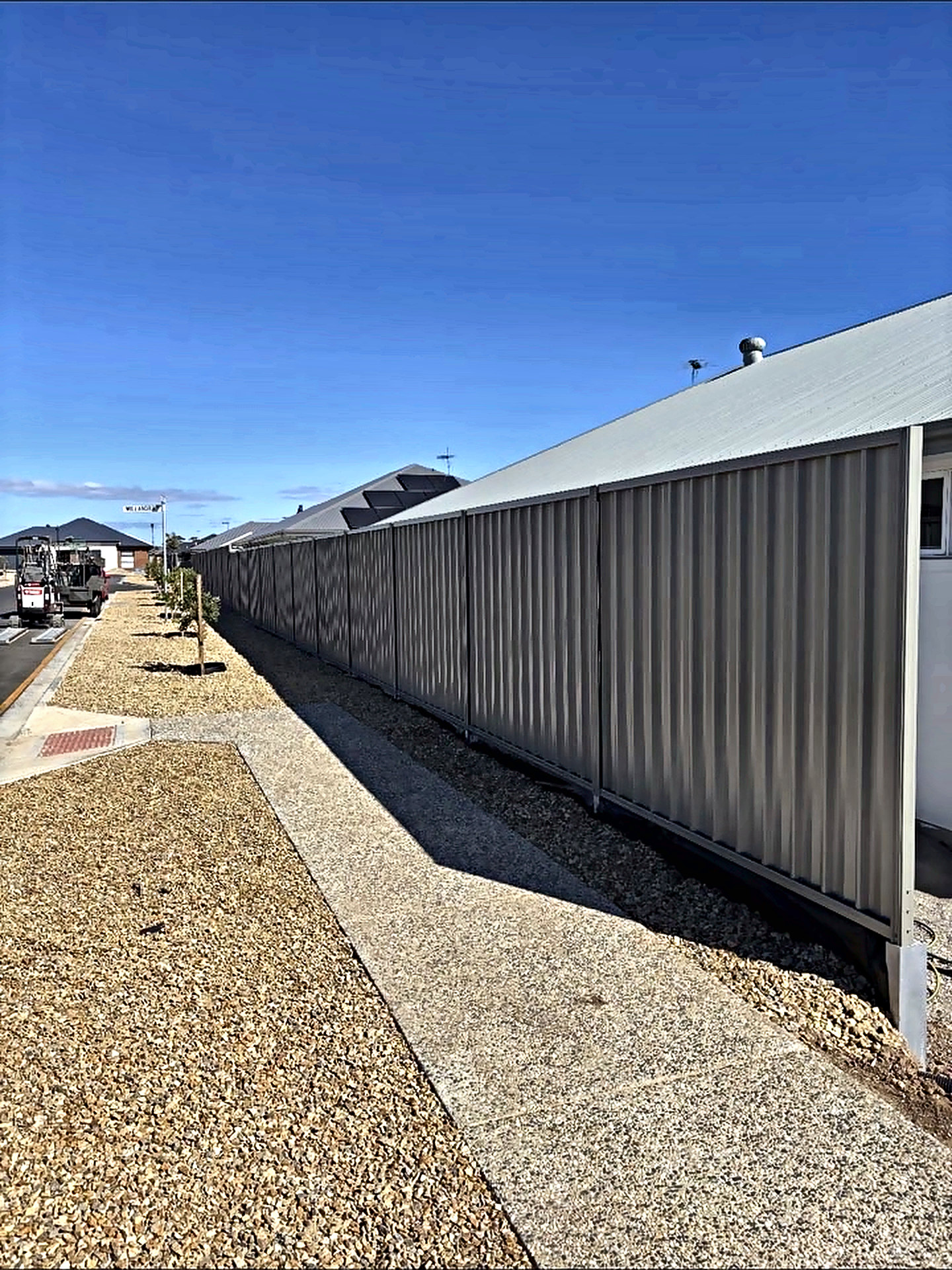 Boundary fence line running the length of a house, with gravel margin and a concrete path under clear sky.